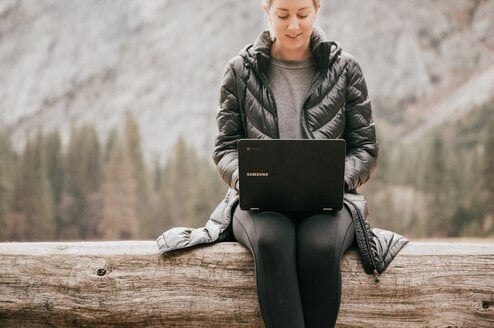 Person sitting on tree log while using laptop