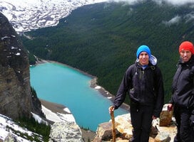 a girl stands on a ledge over looking a lake in the mountains