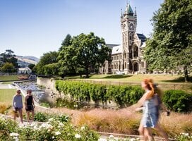 A couple young students walk on campus by a gothic building