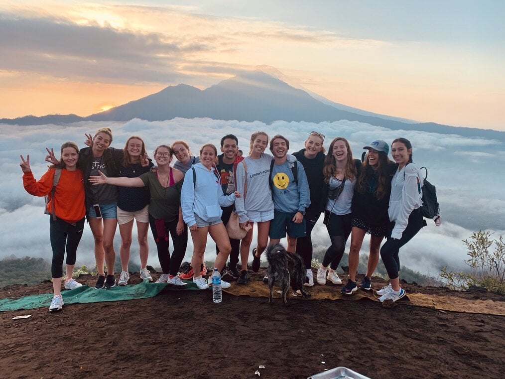 A group of smiling people stand with a mountain in the background.