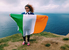 A student poses on a cliff with the Irish flag