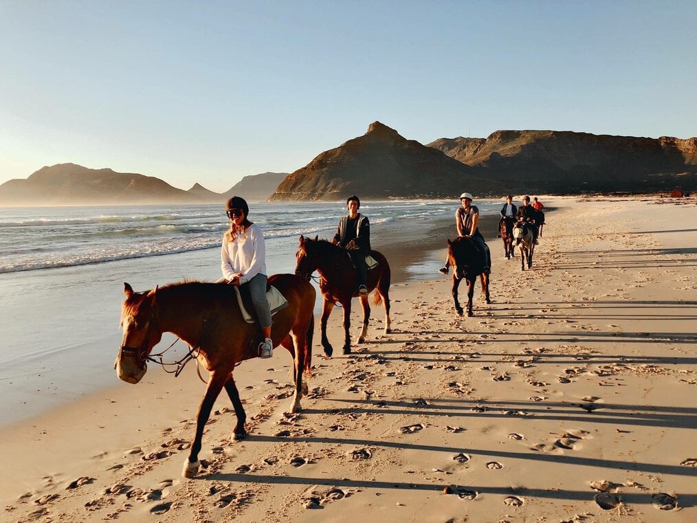 A group of people ride horses along a beach.