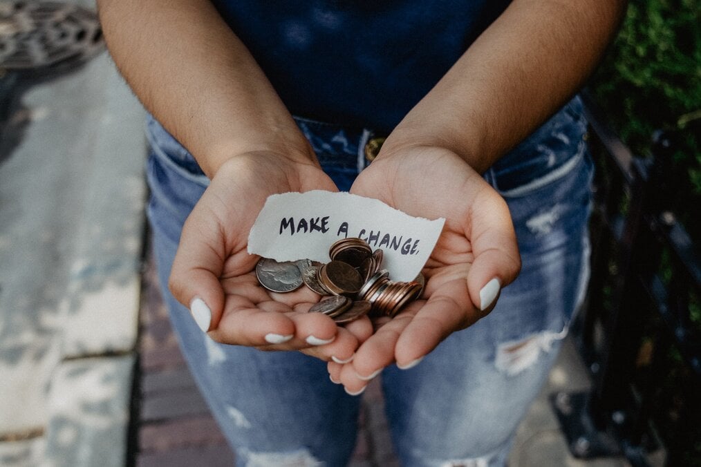 Hands hold coins and a note that says, "make a change".