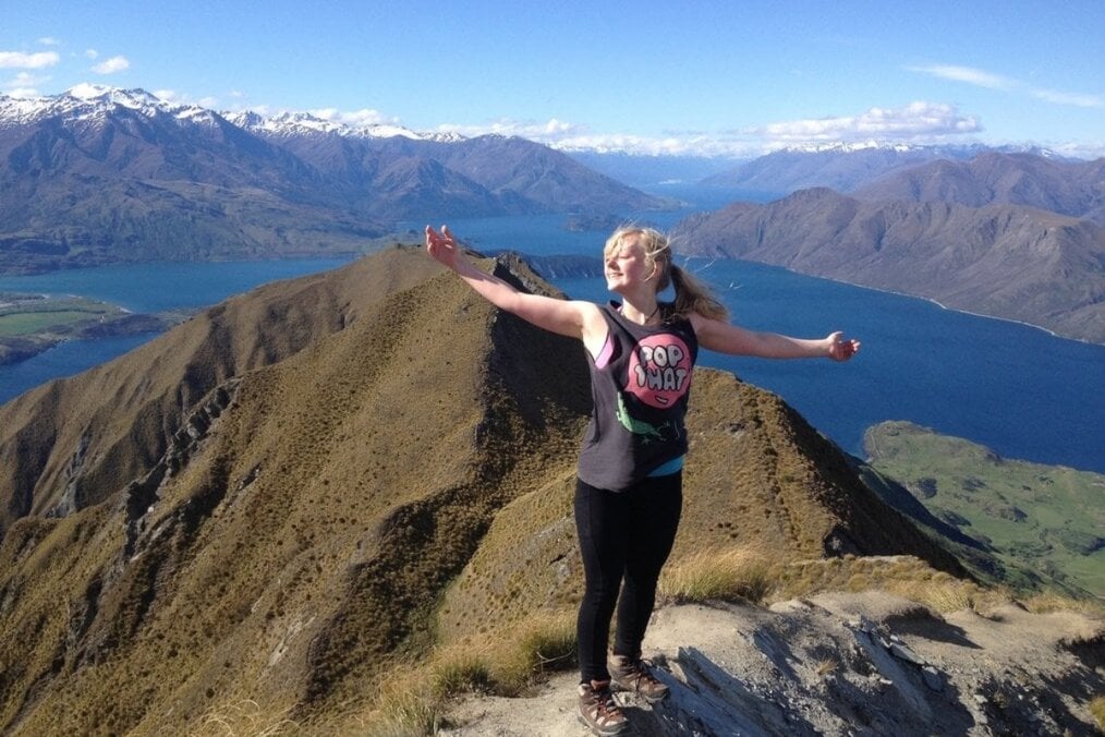 A person standing on top of mountains next to a body of water 