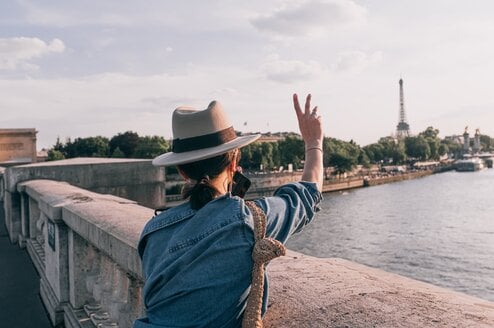 A woman with her back to the camera making a peace sign in the air.