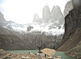 student throwing their arms up while standing on a rock with a vast mountain landscape behind them