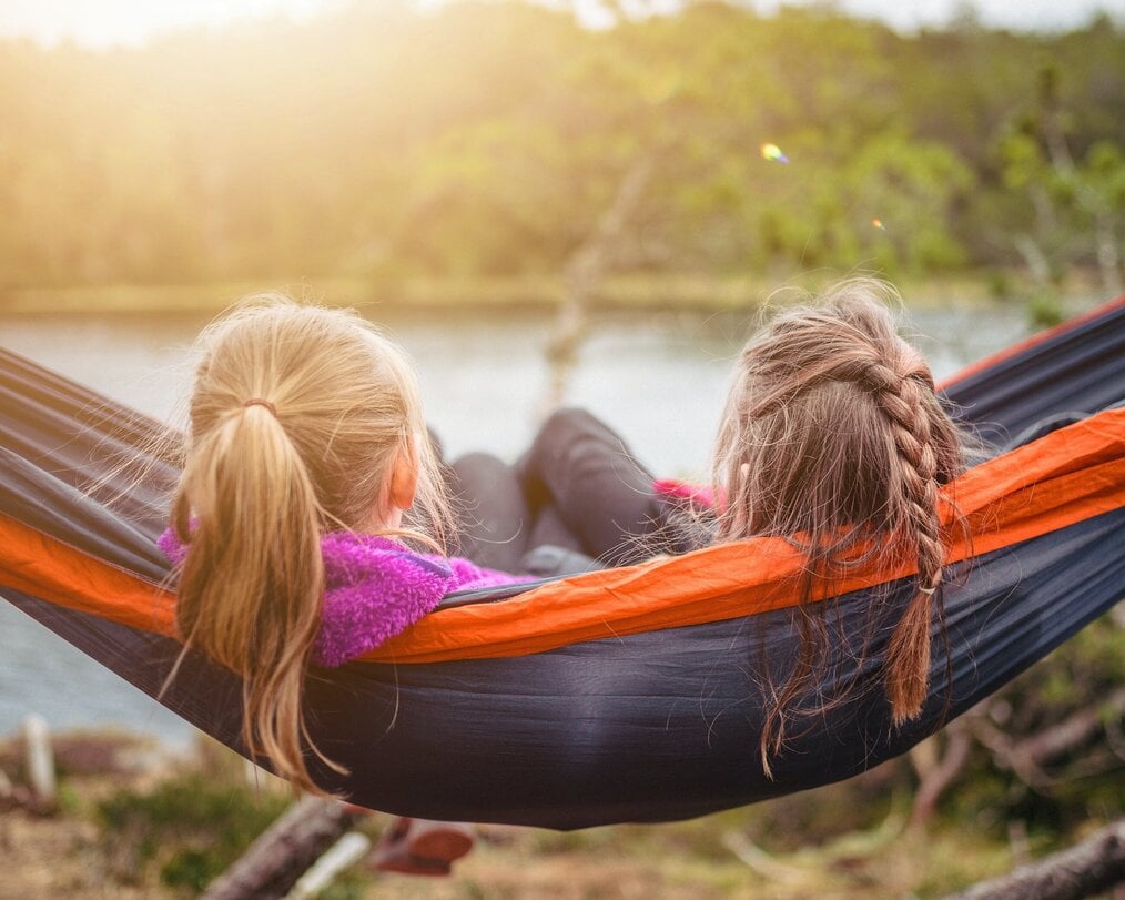 2 people outside sitting in a hammock overlooking water