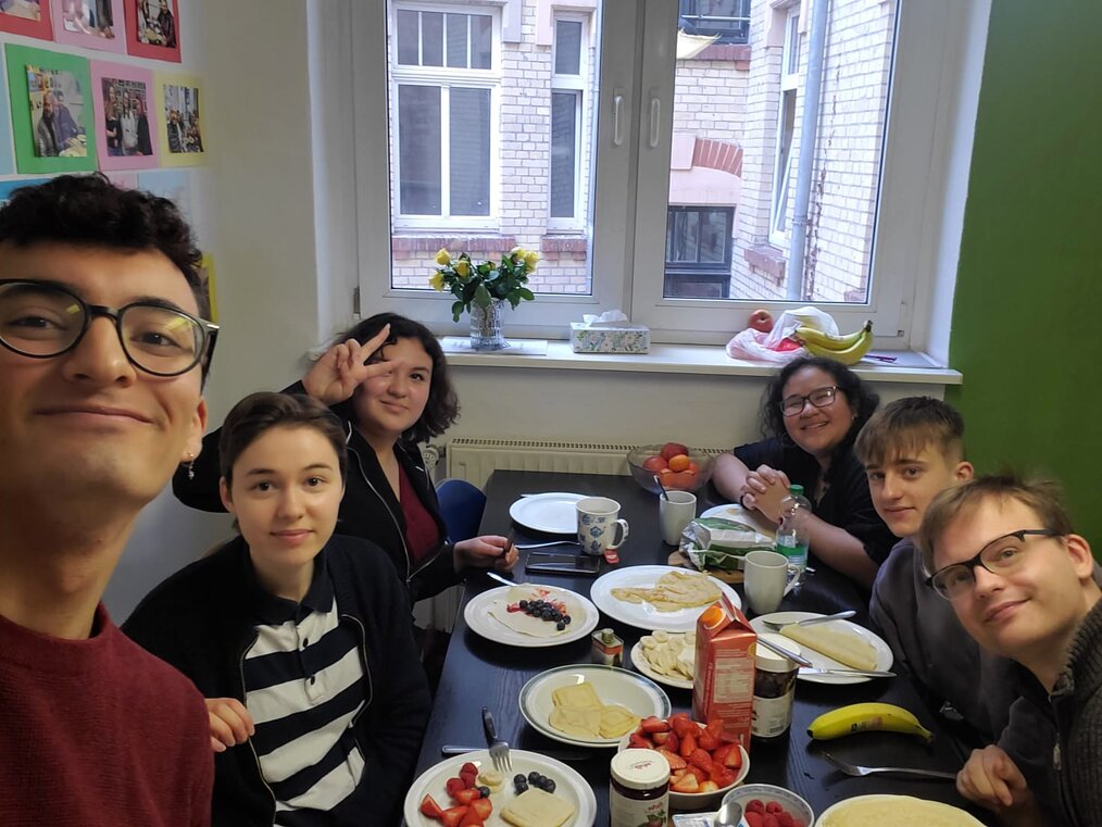 Several people sit and smile at a table with breakfast food on it.